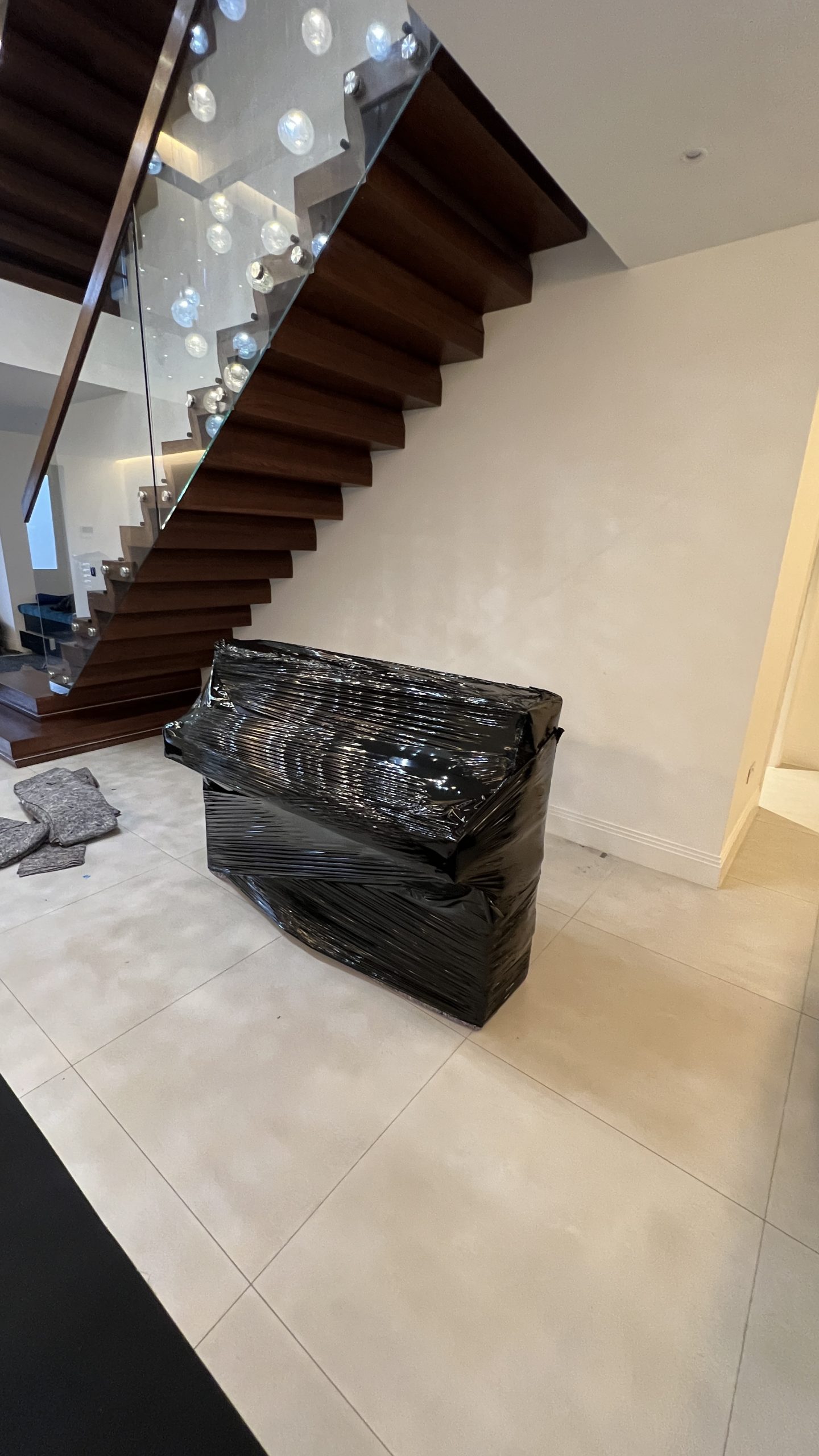 Piano wrapped in black protective covering beside a staircase